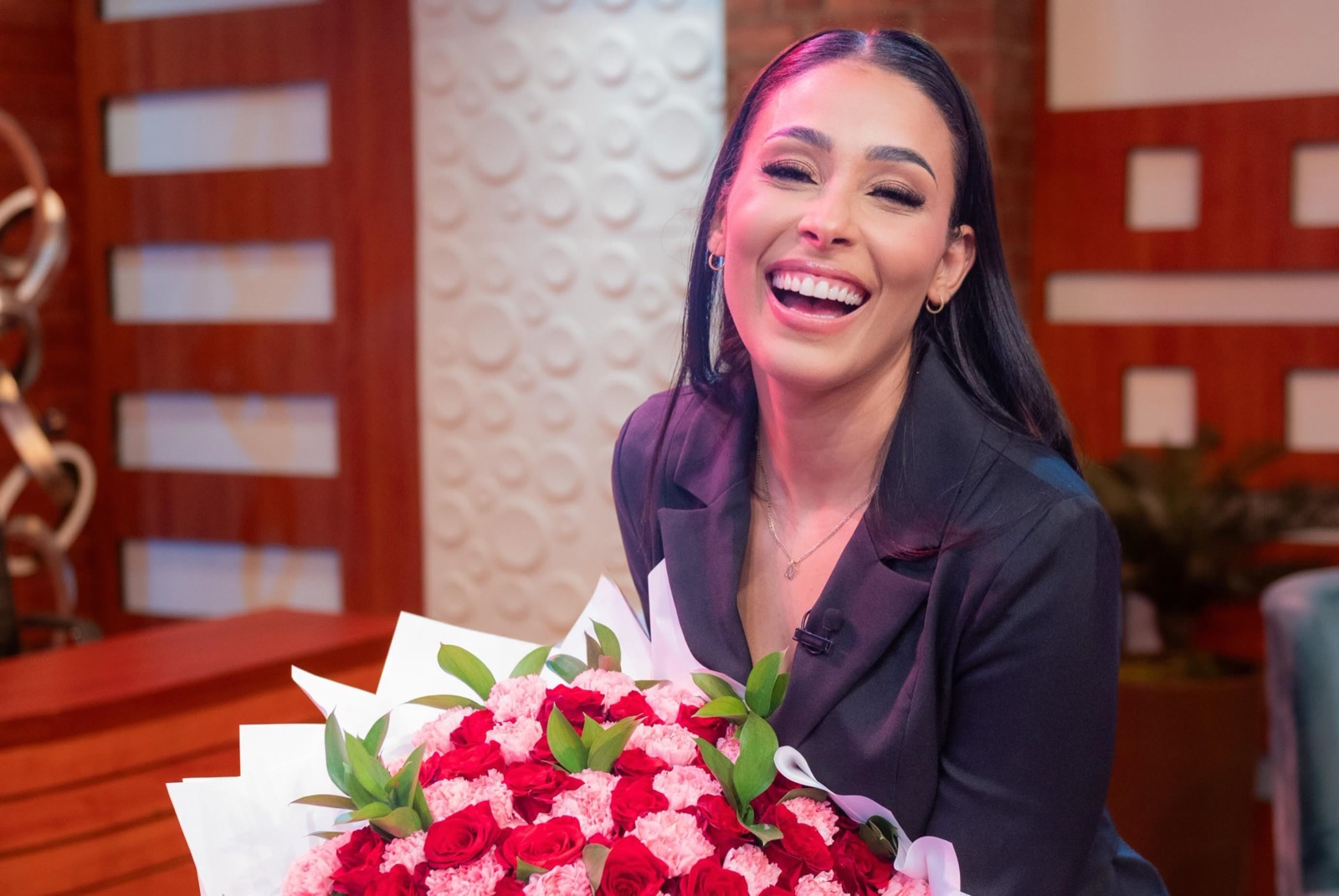 Nelfa riendo en un set de televisión con un ramo de flores
